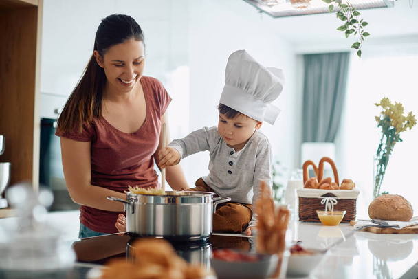 Cute kid wearing chef's hat and cooking with his mother in the kitchen.  - Foto, Imagem