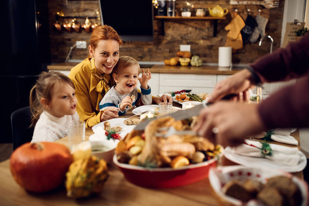 Onnellinen äiti ja lapset nauttivat, kun isä on veistämällä kiitospäivän kalkkuna ruokapöydässä. - Valokuva, kuva