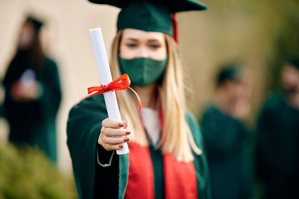 Close-up of college student holding diploma on her graduation day during COVID-19 pandemic. - Photo, Image