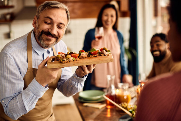 Happy mid adult man serving healthy bruschetta while having a meal with friends at home.  - Foto, Imagem