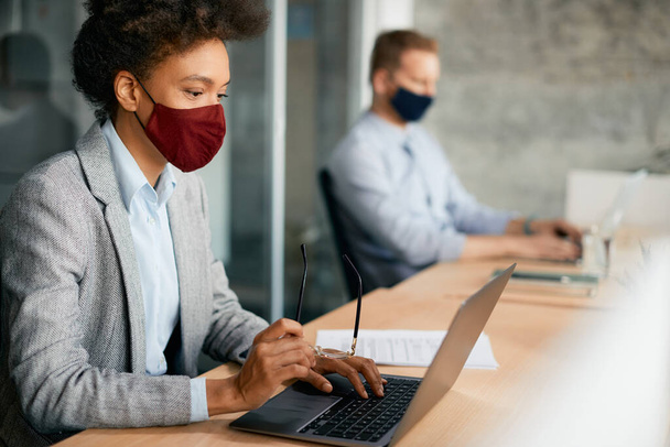 African American businesswoman reading an e-mail on a computer and wearing protective face mask while working in the office. - Φωτογραφία, εικόνα