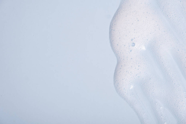 Échantillon de mousse nettoyante visage. Bulles de mousse nettoyante blanche sur fond bleu. Savon, gel douche, shampooing texture mousse gros plan. - Photo, image