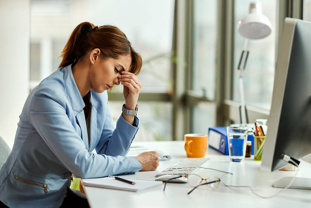 Young displeased businesswoman holding her head in pain while working in the office. - Foto, immagini