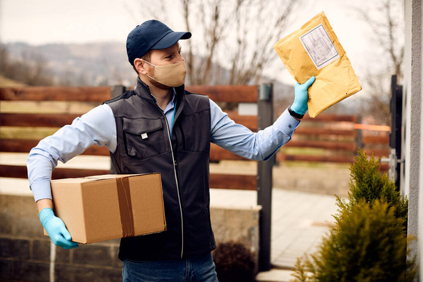 Male courier making delivery to customer's home and wearing protective face mask and gloves due to coronavirus pandemic.  - Fotoğraf, Görsel