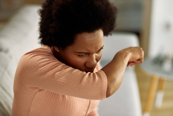 African American woman coughing into her elbow at home. - Foto, Imagem
