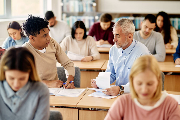 Зрелый профессор ассистирует своему афроамериканскому студенту с лекцией во время занятий в классе. - Фото, изображение
