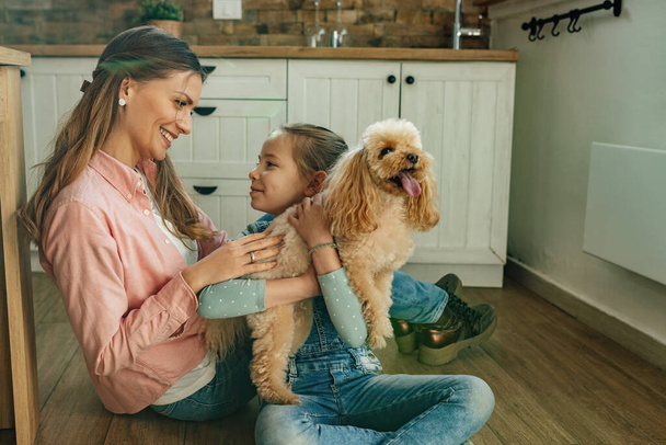 Happy little girl holding her dog while communicating with mother at home.  - 写真・画像