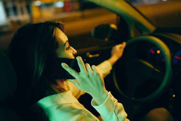 Detailní záběr šťastné ženy telefonovat přes mobilní telefon při řízení auta v noci. - Fotografie, Obrázek