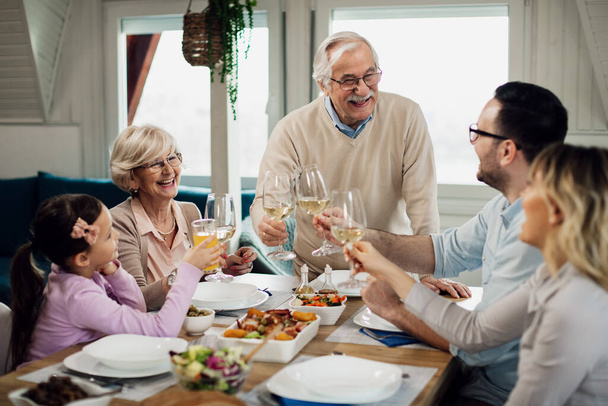 Happy multi-generation family toasting during lunch time at dining table. Focus is on senior couple.  - Foto, imagen