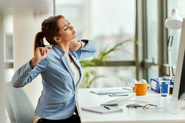 Young businesswoman feeling tired and stretching her neck while working at office desk.  - Foto, Bild
