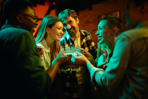 Nuoret onnelliset ihmiset paahtavat ja pitävät hauskaa yöllä baarissa. - Valokuva, kuva