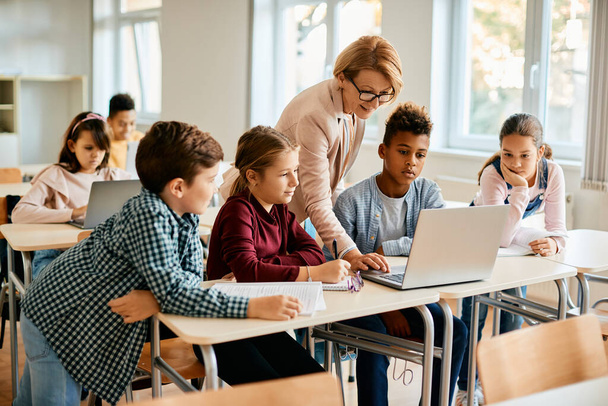 Elementary teacher and her students using laptop during computer class at school. - Fotoğraf, Görsel