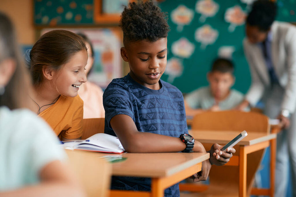 Афроамериканський школяр і його однокласник таємно користуються смартфоном під час занять у класі.. - Фото, зображення