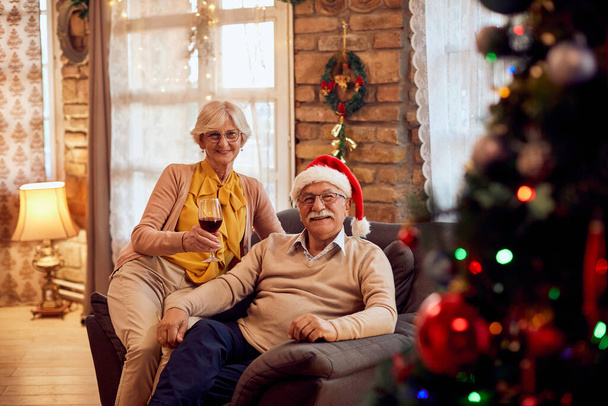 Happy senior woman having a glass of wine while relaxing with her husband on Christmas day at home.  - Foto, Imagen