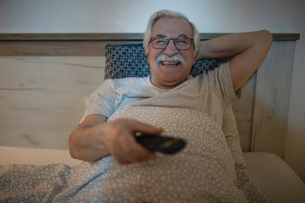 Boldog felnőtt férfi pihen az ágyban és tévézik este.  - Fotó, kép