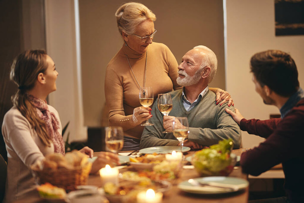 Щаслива старша пара святкує річницю та тости з вином під час сімейної вечері за обіднім столом
.  - Фото, зображення