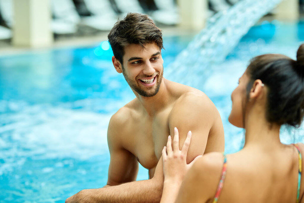 Young happy couple communicating while relaxing by the pool at the spa. Focus is on man. - 写真・画像