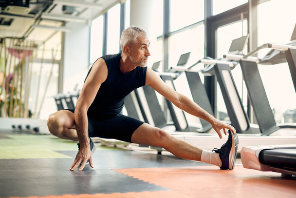 Mature sportsman stretches his leg while warming up in gym. - Фото, зображення