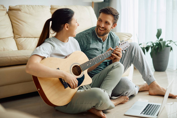 Молодий щасливий чоловік співає з дружиною, поки вона грає на акустичній гітарі вдома
. - Фото, зображення