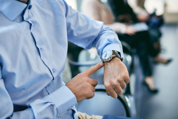 Крупним планом бізнесмен вказує вчасно на наручний годинник, сидячи в залі очікування
. - Фото, зображення
