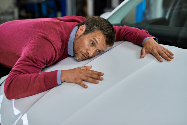 Mid adult man feeling relived and leaning on car hood in auto repair shop.  - Foto, immagini