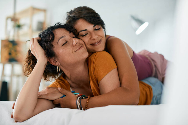 Young lesbian couple in love embracing with their eyes closed while relaxing on a bed.  - Foto, afbeelding