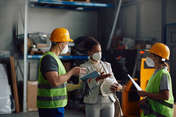 Two warehouse workers communicating with African American manager at storage compartment. They are wearing face masks due to coronavirus pandemic.  - Foto, Imagem