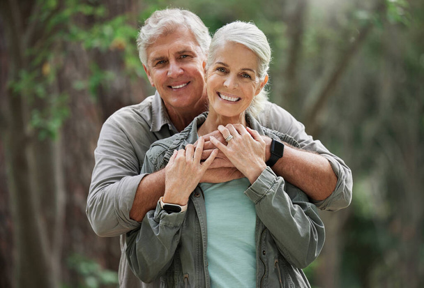 Retrato de una pareja de ancianos caucásicos sonriendo y luciendo felices en un bosque durante una caminata al aire libre. Hombre y mujer mostrando afecto y abrazándose durante una pausa en la naturaleza. - Foto, imagen