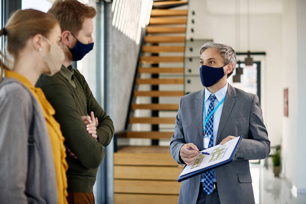 Real estate agent and couple wearing face masks while goring through blue prints of a new apartment.  - Fotoğraf, Görsel