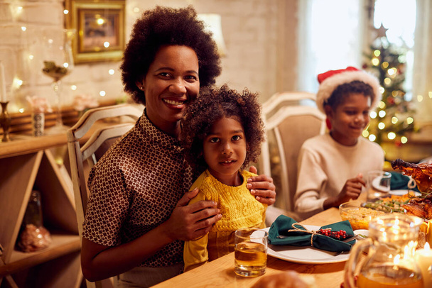 Happy African American mother with children enjoying in Christmas lunch at dining table and looking at camera.  - Zdjęcie, obraz