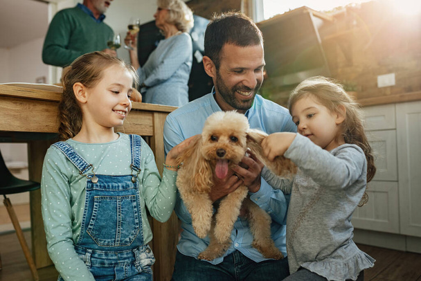Дві маленькі дівчата та їх батько насолоджуються собакою вдома
.  - Фото, зображення