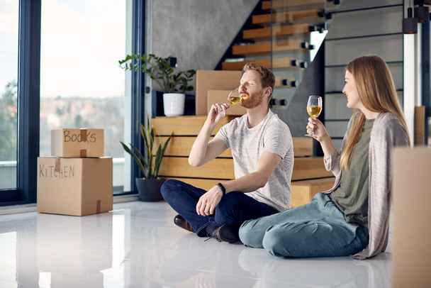 Young couple drinking wine after moving in their new home. Focus is on man drinking with eyes closed.  - Valokuva, kuva