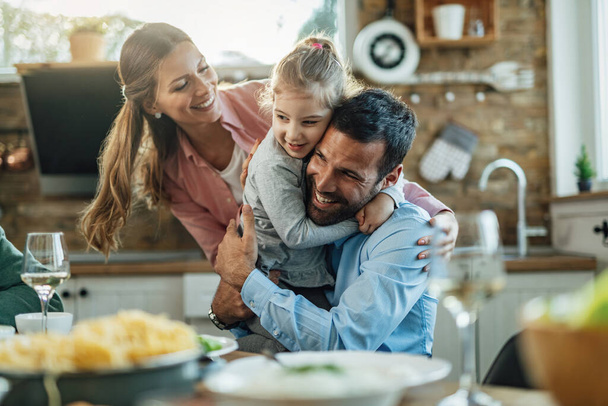 Young happy parents embracing with their small daughter during lunch at dining table.  - 写真・画像