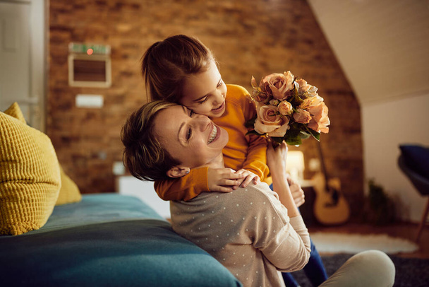 Mutlu anne evde çiçek alırken kızını kucaklıyor..  - Fotoğraf, Görsel
