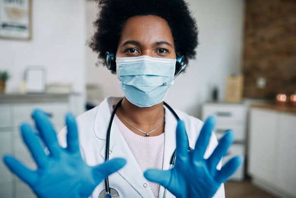 Black female doctor wearing protective face mask and gloves while having conference call and looking at camera. - Foto, imagen