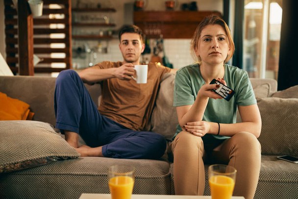 Young woman feeling bored and changing channels while watching TV with her boyfriend at home. - Φωτογραφία, εικόνα