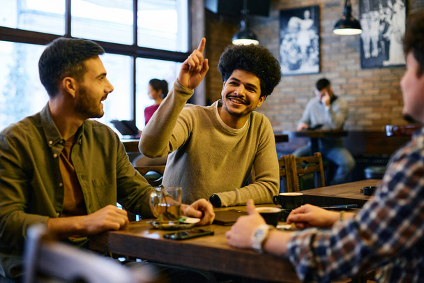 Group of multiracial friends making order in a pub. Focus is on Lebanese man with hand raised calling the waiter. - Foto, imagen