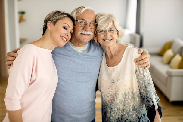 Portrait of happy senior parents and their adult daughter standing embraced  at home.  - Fotoğraf, Görsel