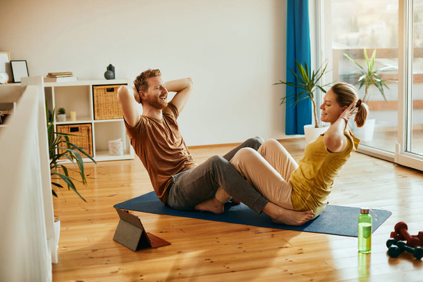 Young happy couple exercising crunches while working out together at home.  - Fotó, kép