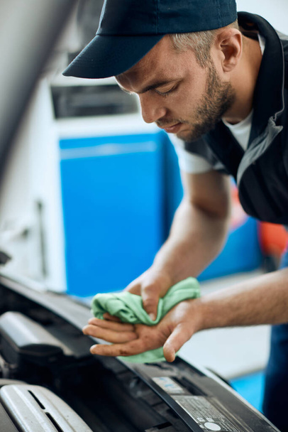 Young mechanic cleaning hands after repairing car engine at auto service shop.  - Photo, image
