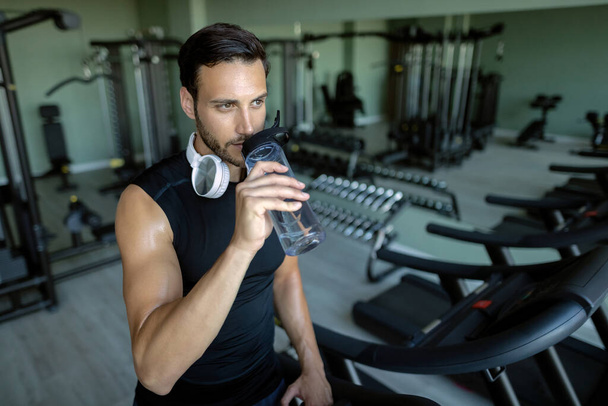 Pensive sportsman refreshing himself and drinking water while exercising in a gym . - Foto, imagen