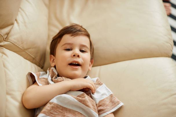Cute small boy lying down on sofa at home and looking at camera.  - Foto, afbeelding