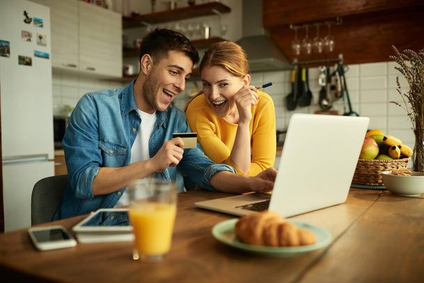 Young happy couple using laptop and credit card while shopping on the internet at home.  - Photo, image