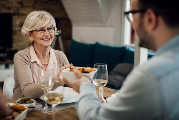 Happy mature woman eating with her adult son and passing him food at dining table.  - Photo, image