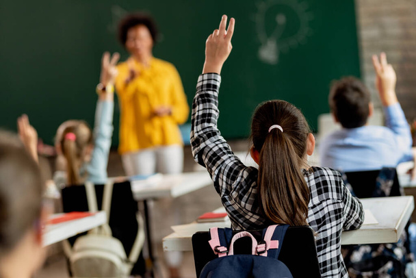 Back view of elementary student raising arm in order to answer a questing during a class.  - 写真・画像