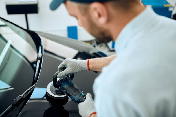 Close-up of mechanic polishing car hood while working in a workshop.  - Фото, изображение