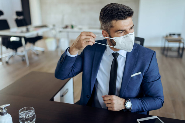 Young businessman working in the office and putting on a face mask due to coronavirus epidemic.  - Fotó, kép