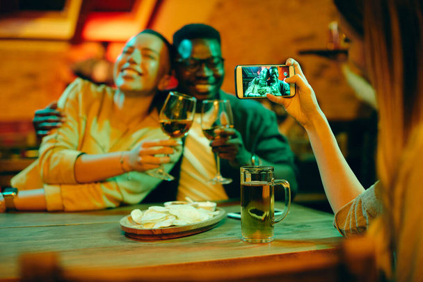 Close-up of woman taking picture of African American couple during their night out in a bar. - Fotó, kép