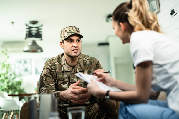 Young military man talking to healthcare worker who is visiting him at home.  - Φωτογραφία, εικόνα