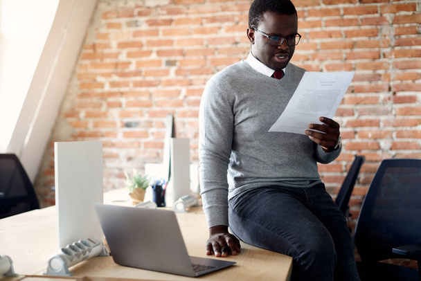 Афроамериканський бізнесмен аналізує документи, сидячи на своєму офісному столі.. - Фото, зображення